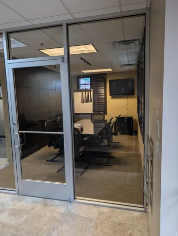 Glass-paneled entry door, commercial-grade carpet, suspended ceiling with recessed lighting, and wall-mounted screen