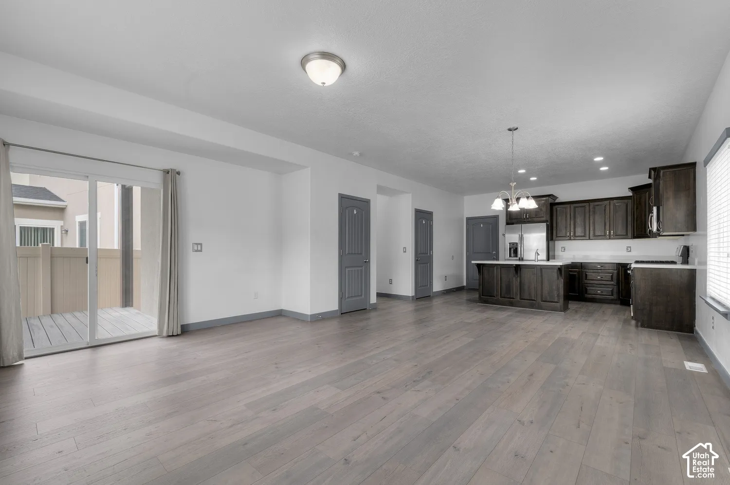 Spacious open concept living area with wood-finish flooring, a kitchen featuring dark wood cabinetry, white countertops, and stainless steel appliances