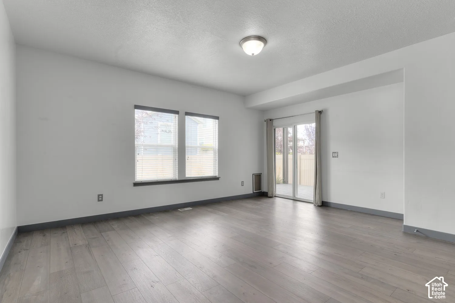 Wood-finish flooring, multiple windows with blinds, sliding glass door, recessed lighting, and a neutral color palette