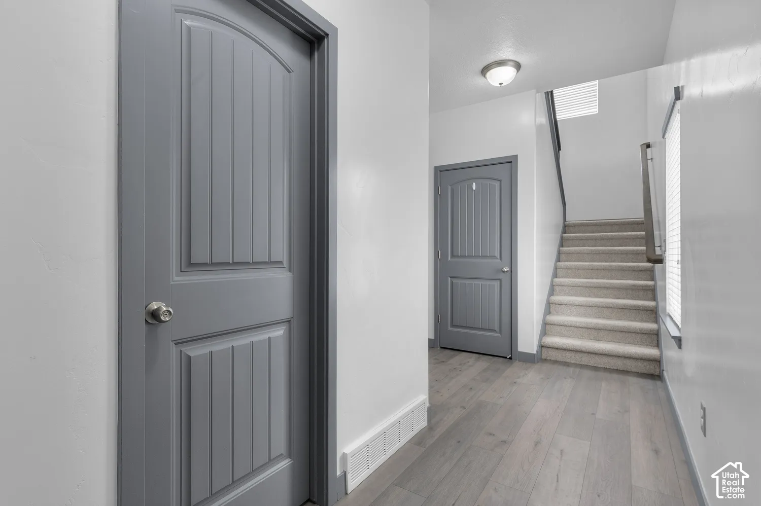 Light gray wood-finish flooring, white walls, gray interior doors with arched top panels, and a carpeted staircase