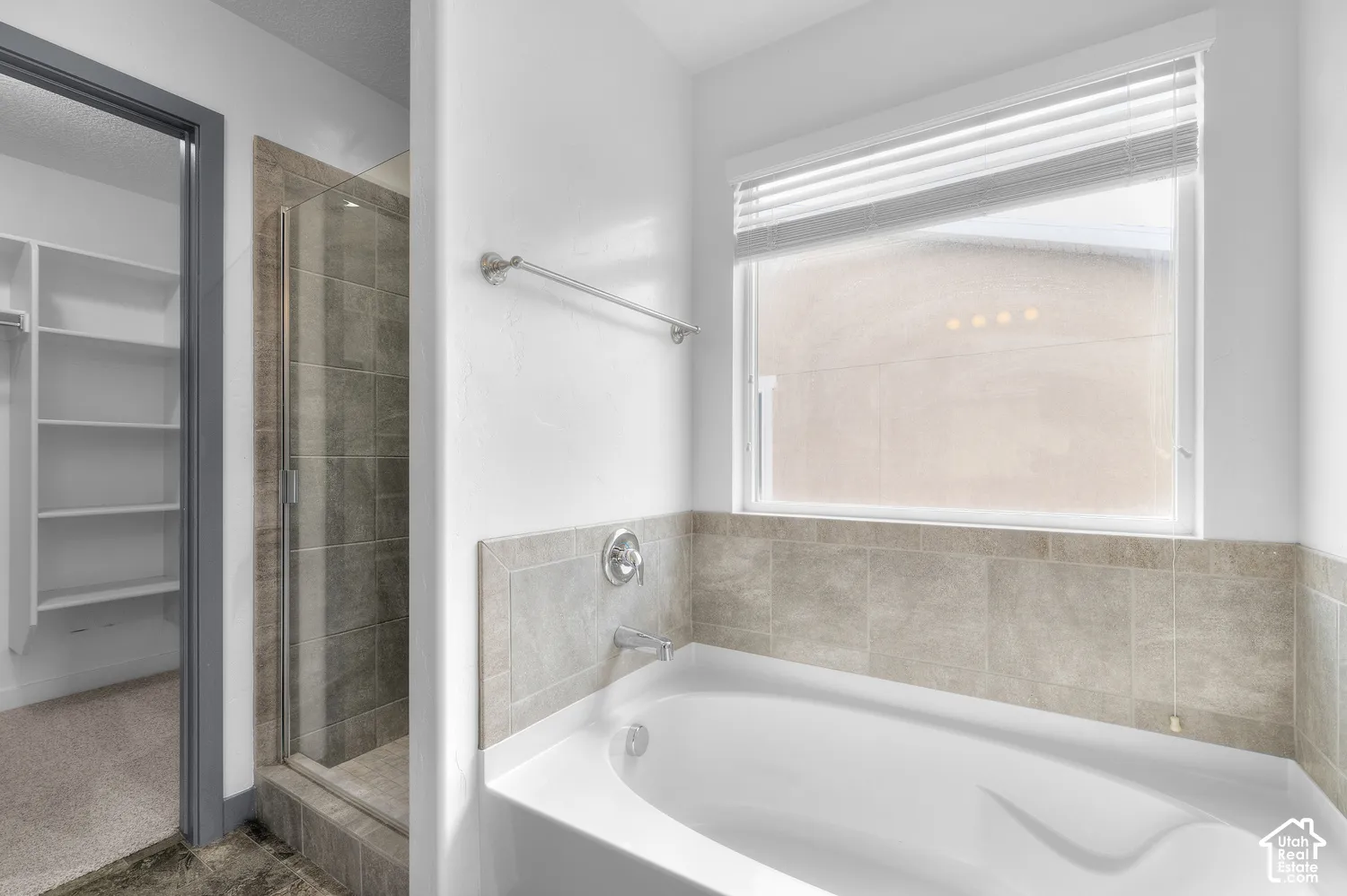 Soaking tub with tile surround, adjacent glass-enclosed shower, and built-in closet shelving
