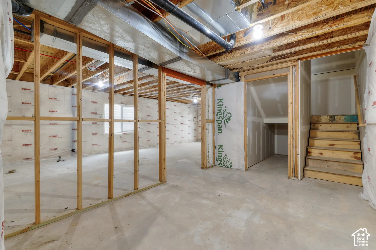 Unfinished lower level featuring concrete flooring, exposed wood framing, and wood stairs