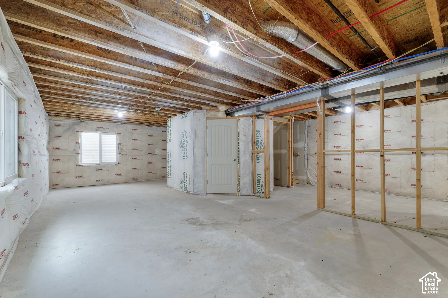 Spacious unfinished basement with exposed wood-beam ceiling, concrete flooring, and framed wall sections ready for customization