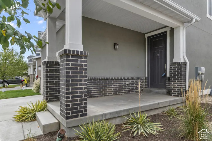 Covered front porch featuring a dark entry door, brick columns, and stucco exterior