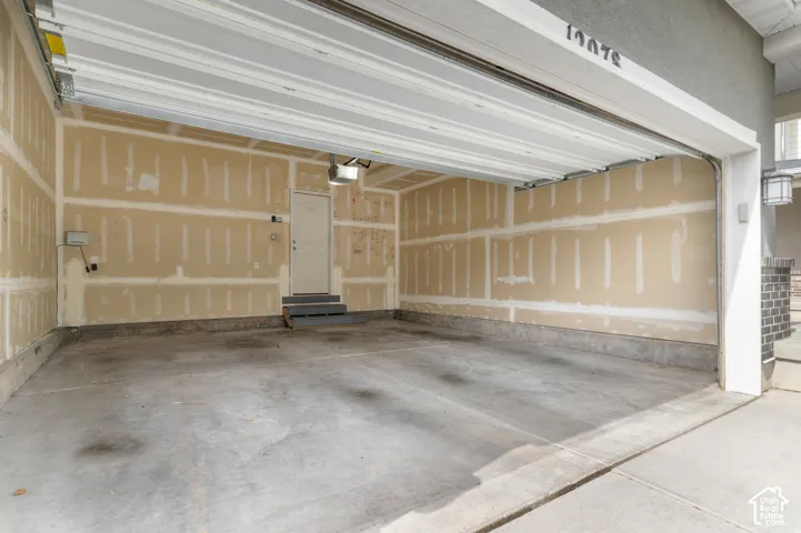 Attached garage with concrete flooring, automatic garage door opener, interior door access, and exterior wall sconce