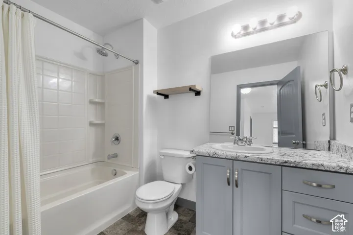 Bathroom featuring a built-in bathtub with shower, white tile surround, gray vanity cabinetry, a countertop with integrated sink, and an overhead vanity light fixture