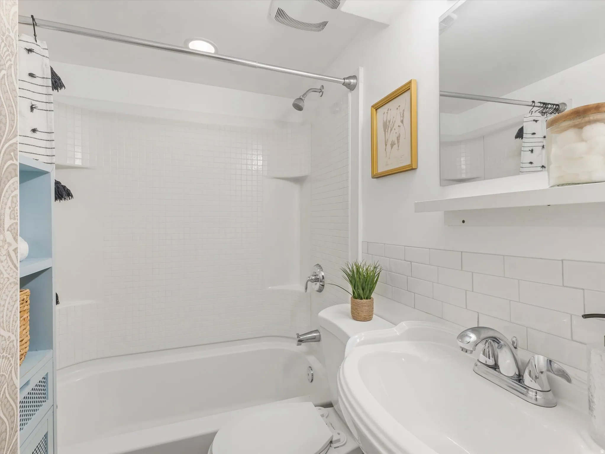 Bathtub with integrated shower, white subway tile wainscoting, and pedestal sink with chrome faucet