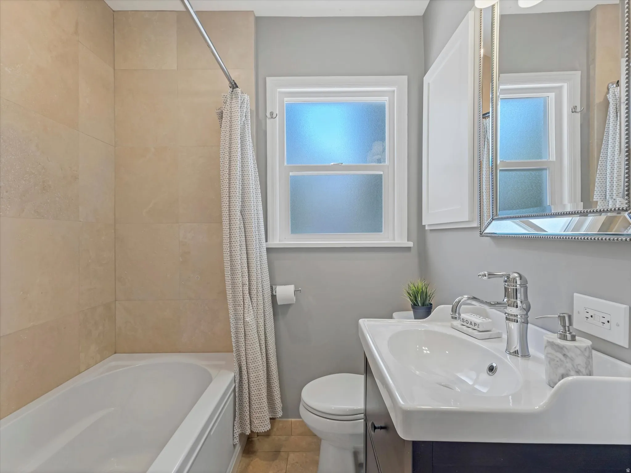 Bathtub with full-height tiled surround, white window frame with frosted glass, built-in medicine cabinet with white door, vanity with integrated basin sink, and chrome fixtures
