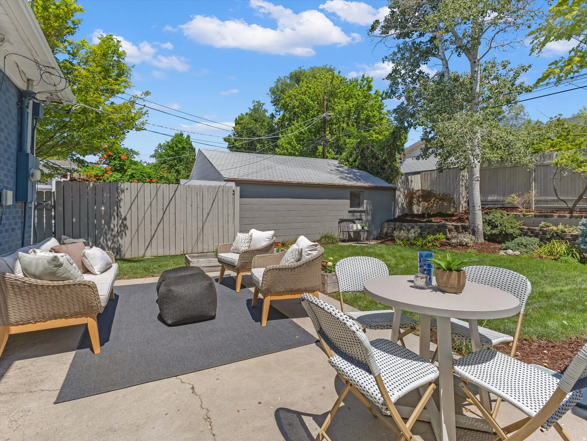 Concrete patio with a gray outdoor rug, expansive lawn, and mature trees