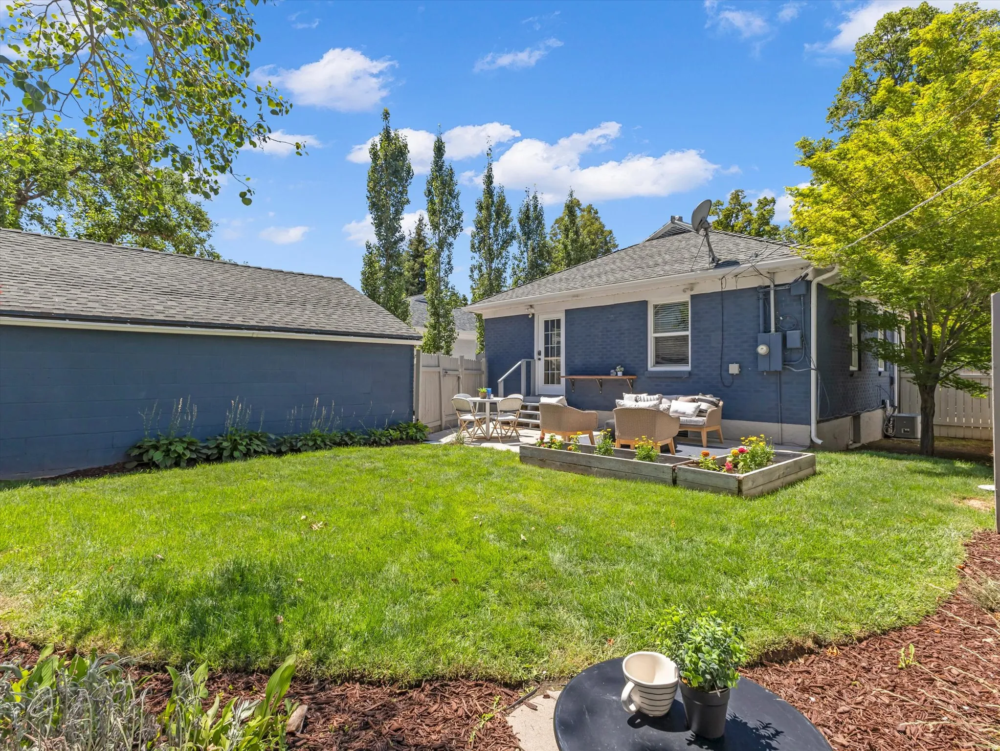 Expansive grassy yard with a detached garage, a paved patio, and raised garden beds