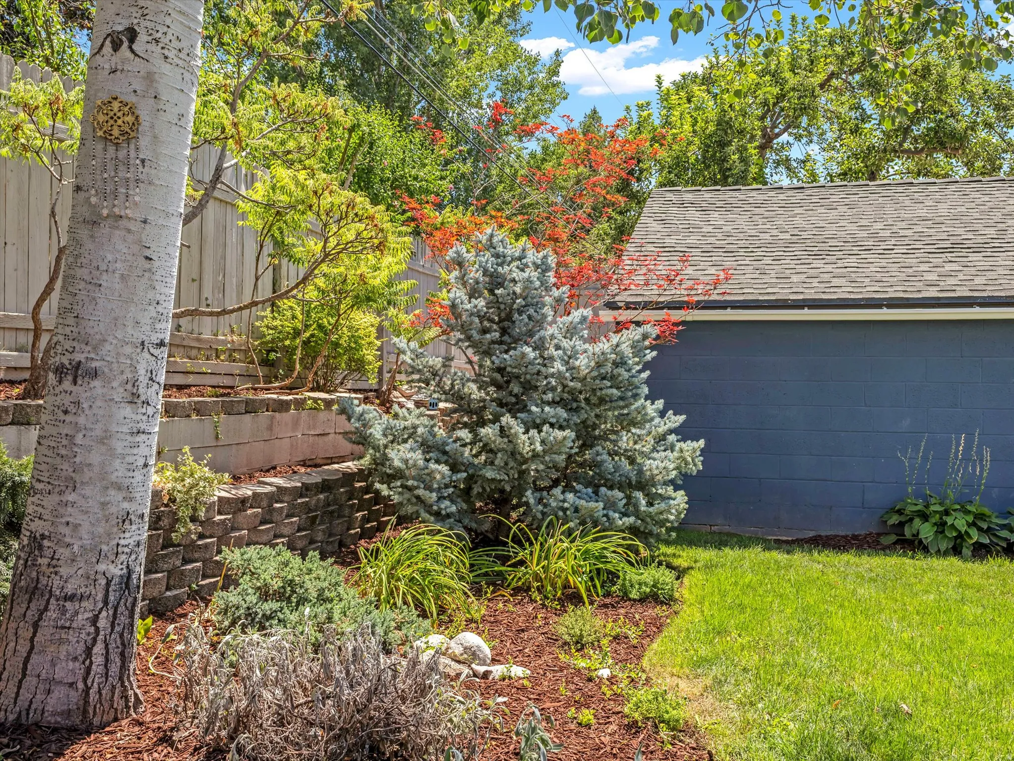 Manicured lawn with a retaining wall, mature trees, and a landscaped garden bed