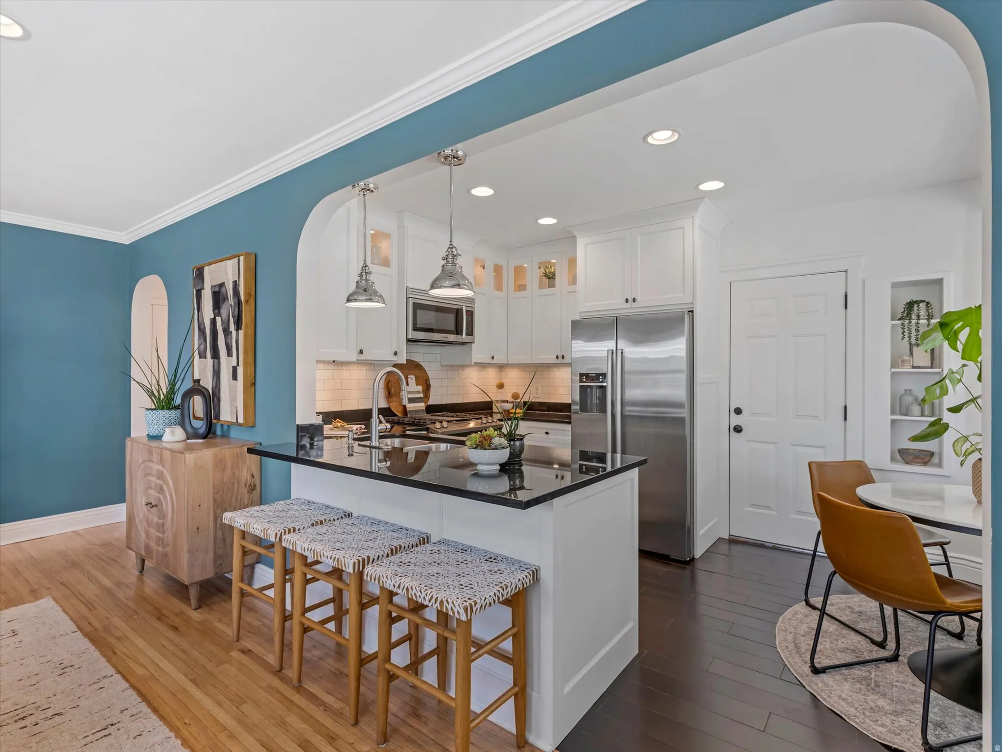 White cabinetry, stainless steel appliances, dark stone countertop, wood-finish flooring, and recessed lighting