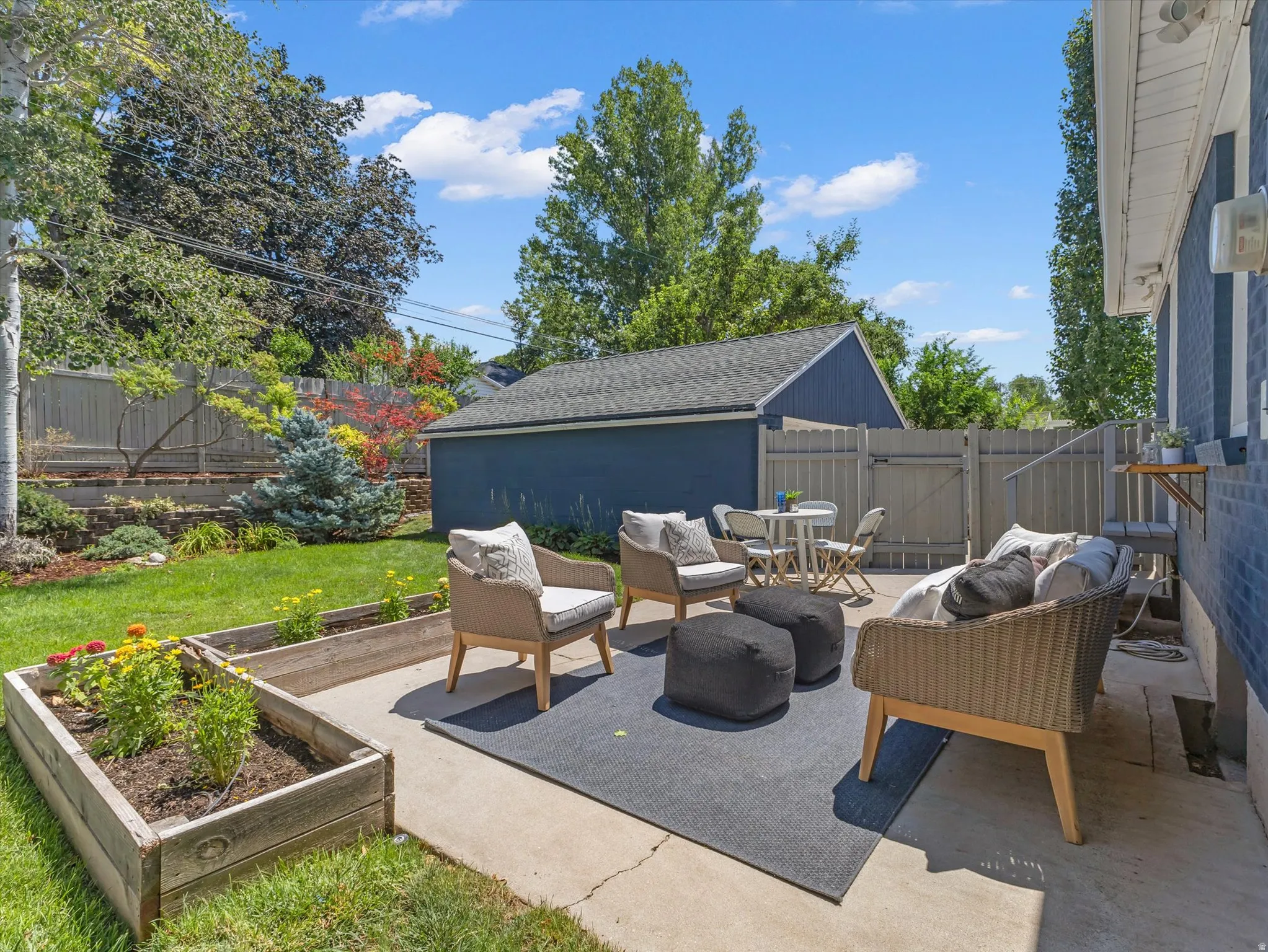 Concrete patio area with a privacy fence, raised garden beds, and mature trees