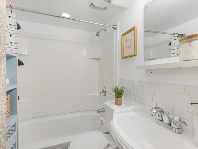 Bathtub with integrated shower, white subway tile wainscoting, and pedestal sink with chrome faucet