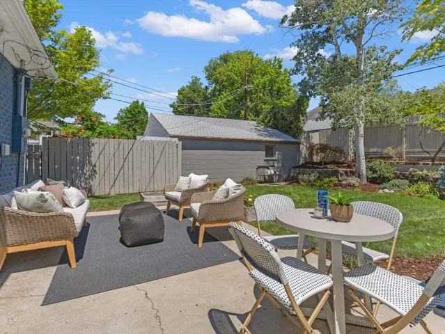 Concrete patio with a gray outdoor rug, expansive lawn, and mature trees