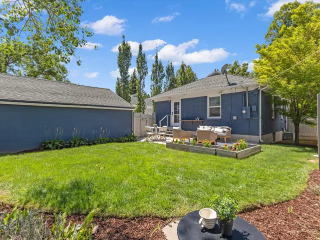 Expansive grassy yard with a detached garage, a paved patio, and raised garden beds