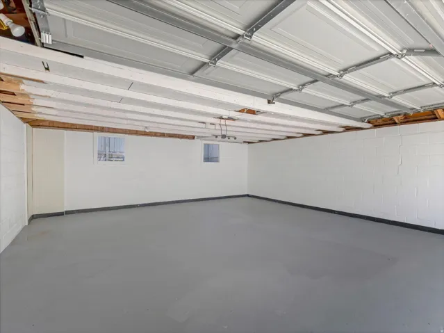 Spacious garage with painted concrete block walls, exposed wood ceiling joists, and a painted concrete floor