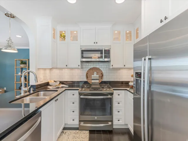 White cabinetry with dark hardware, dark countertops, a subway tile backsplash, and stainless steel appliances