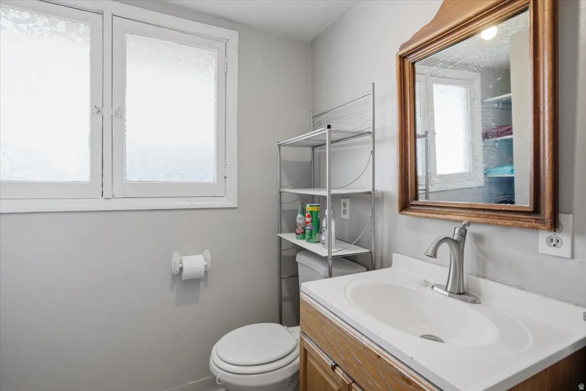 Bathroom featuring a wood-finish vanity with an integrated sink, a wall-mounted mirror with a decorative frame, and a dual-pane window