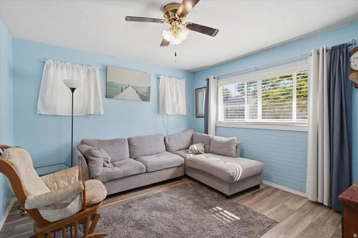Bright and airy living room featuring light blue shiplap walls, a ceiling fan with integrated lighting, and large windows with plantation shutters and layered window treatments