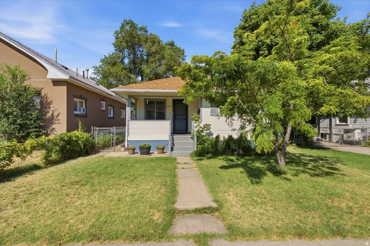 Charming single-story home with a manicured lawn, concrete walkway, and mature shade trees