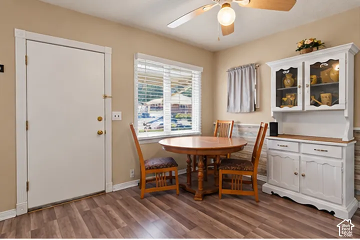 Wood-finish flooring, white built-in cabinetry with glass-front doors, a window with horizontal blinds, a ceiling fan with integrated lighting, and a white interior door