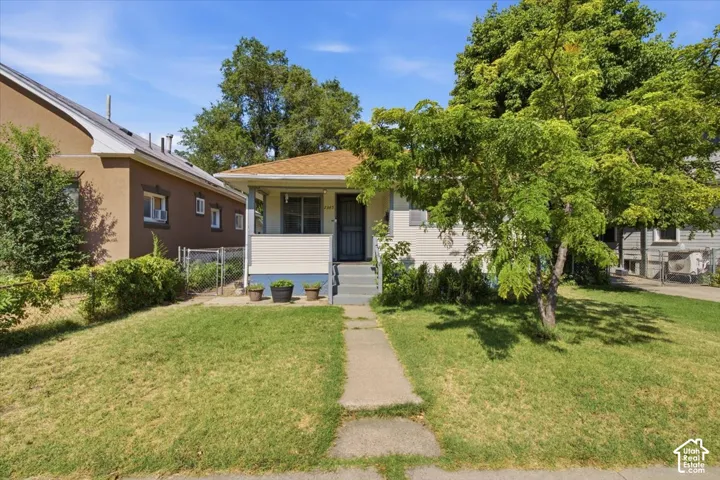 Charming single-story home with a manicured lawn, concrete walkway, and mature shade trees