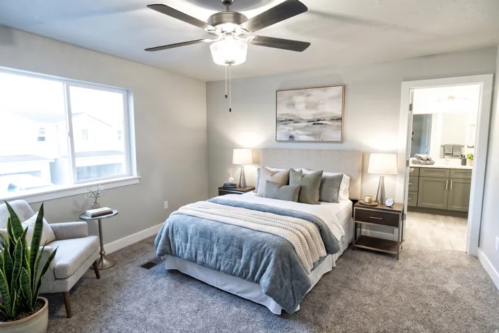 Carpeted room with a ceiling fan light fixture, a large window, and an open doorway to a bathroom