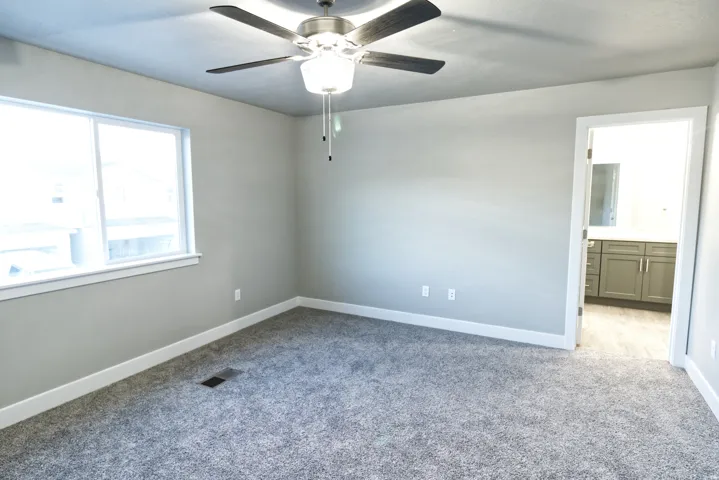 Previous build home - colors and selections may vary. Window with white trim, ceiling fan with light fixture, gray wall paint, gray carpet, and white baseboards