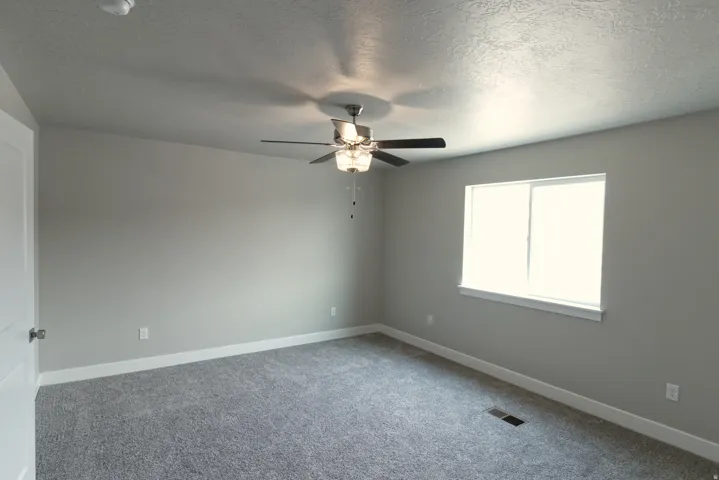 Previous build home - colors and selections may vary. Spacious bedroom with neutral gray walls, carpet flooring, and abundant natural light from a large window