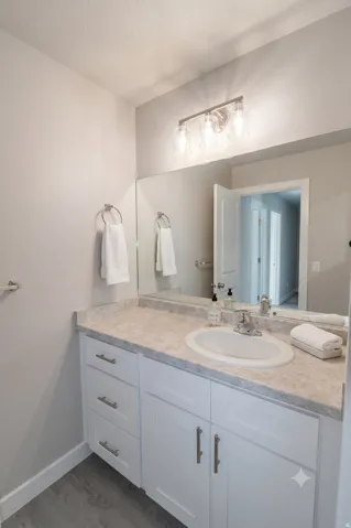 White vanity with brushed nickel hardware, integrated sink, and light-toned countertop, complemented by a large wall-mounted mirror and wood-finish flooring