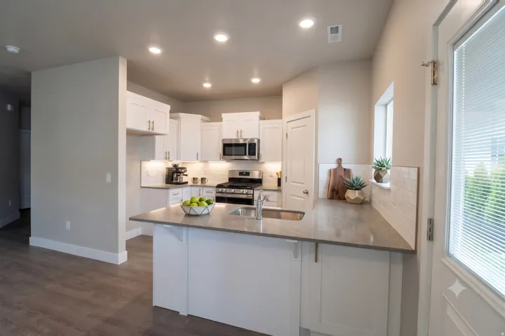 Kitchen featuring white cabinetry, stainless steel appliances, a center island with sink, grey countertops, and wood-finish flooring