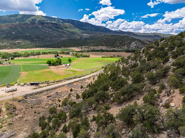 Expansive landscape featuring distant mountains, a broad valley, cultivated green fields, and a hilly foreground with scattered trees
