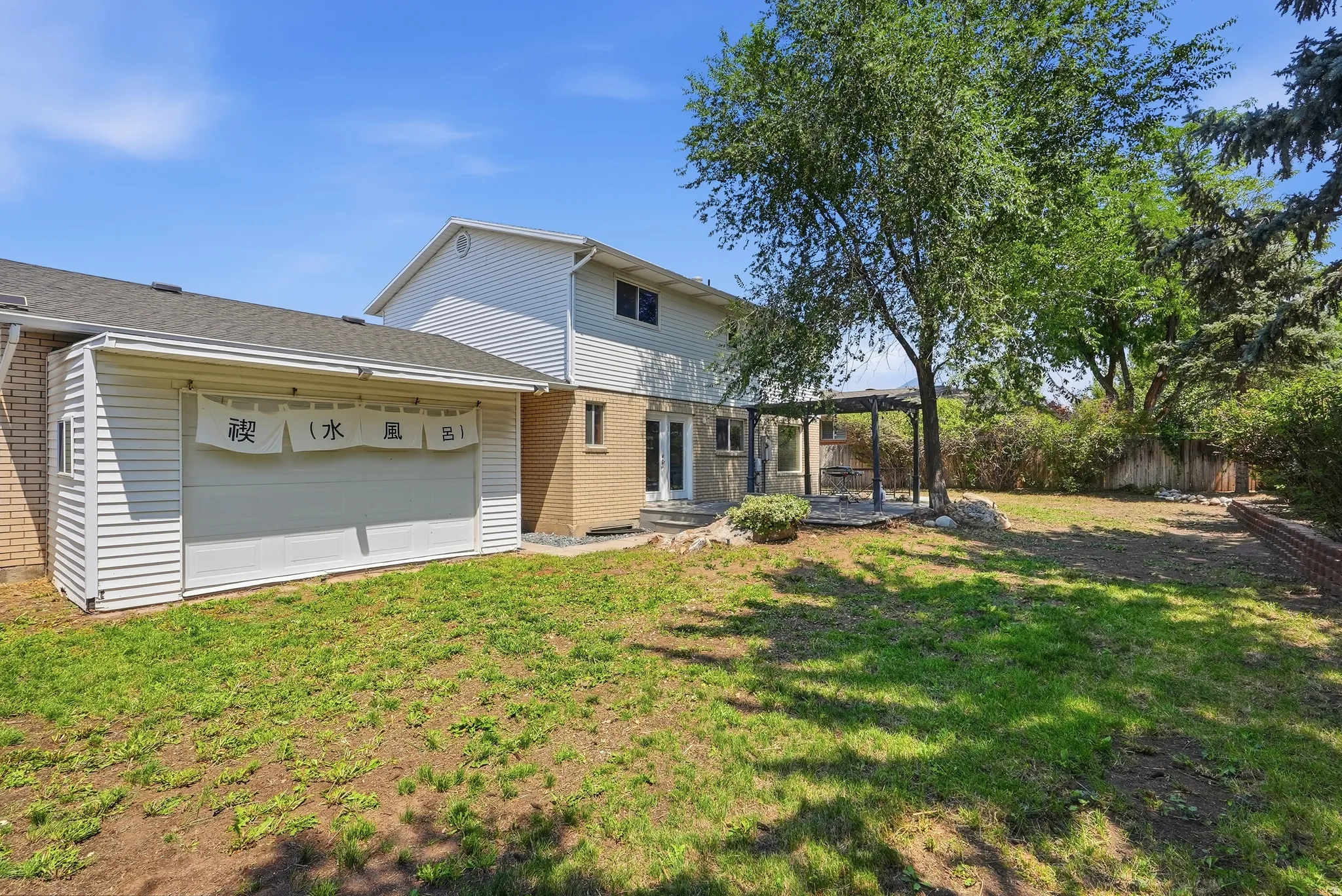 Spacious backyard featuring a pergola, brick retaining wall, and mature trees