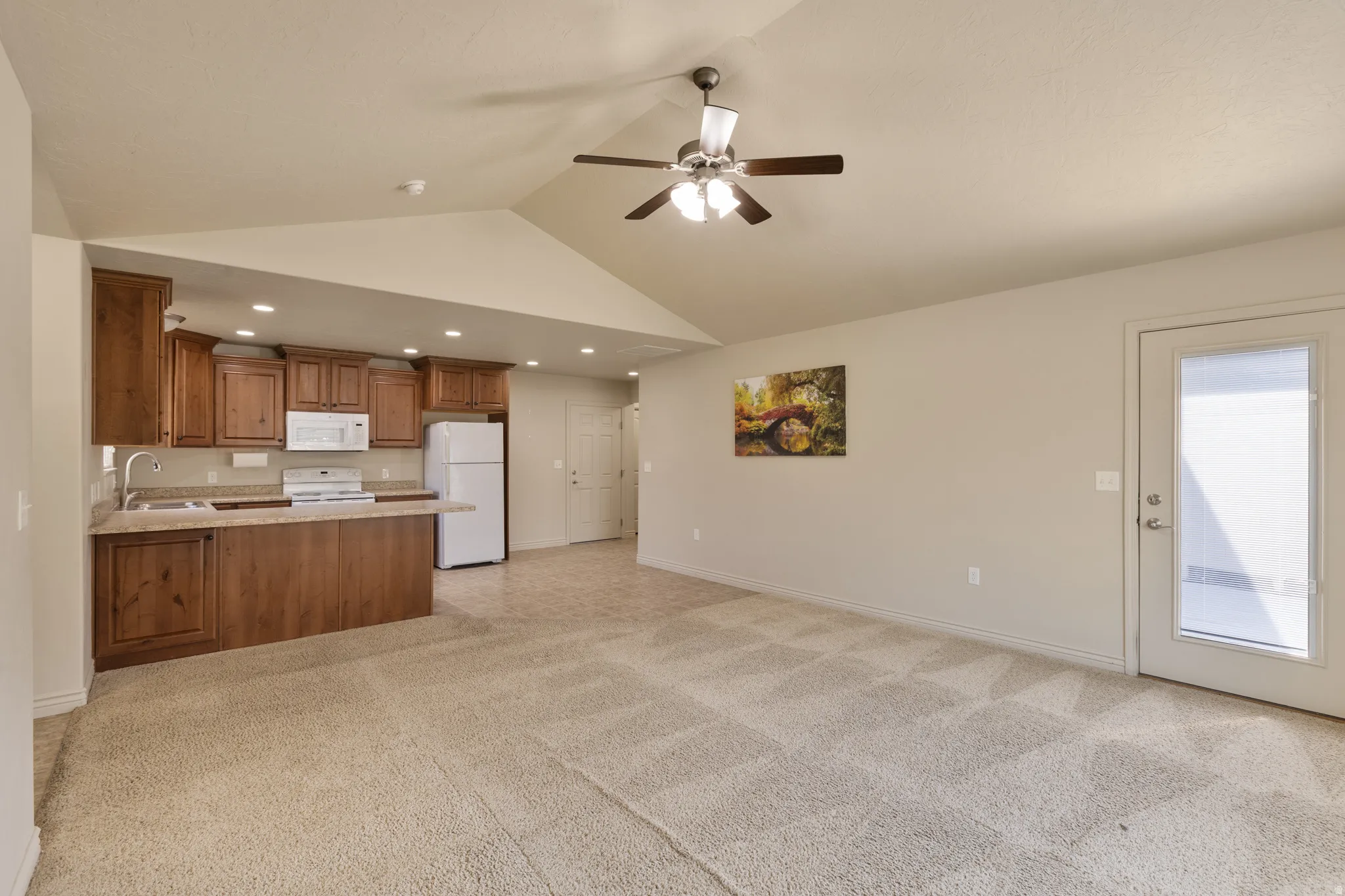 Vaulted ceiling with a ceiling fan, recessed lighting, wood-finish cabinetry, built-in white appliances, and an exterior door with glass paneling