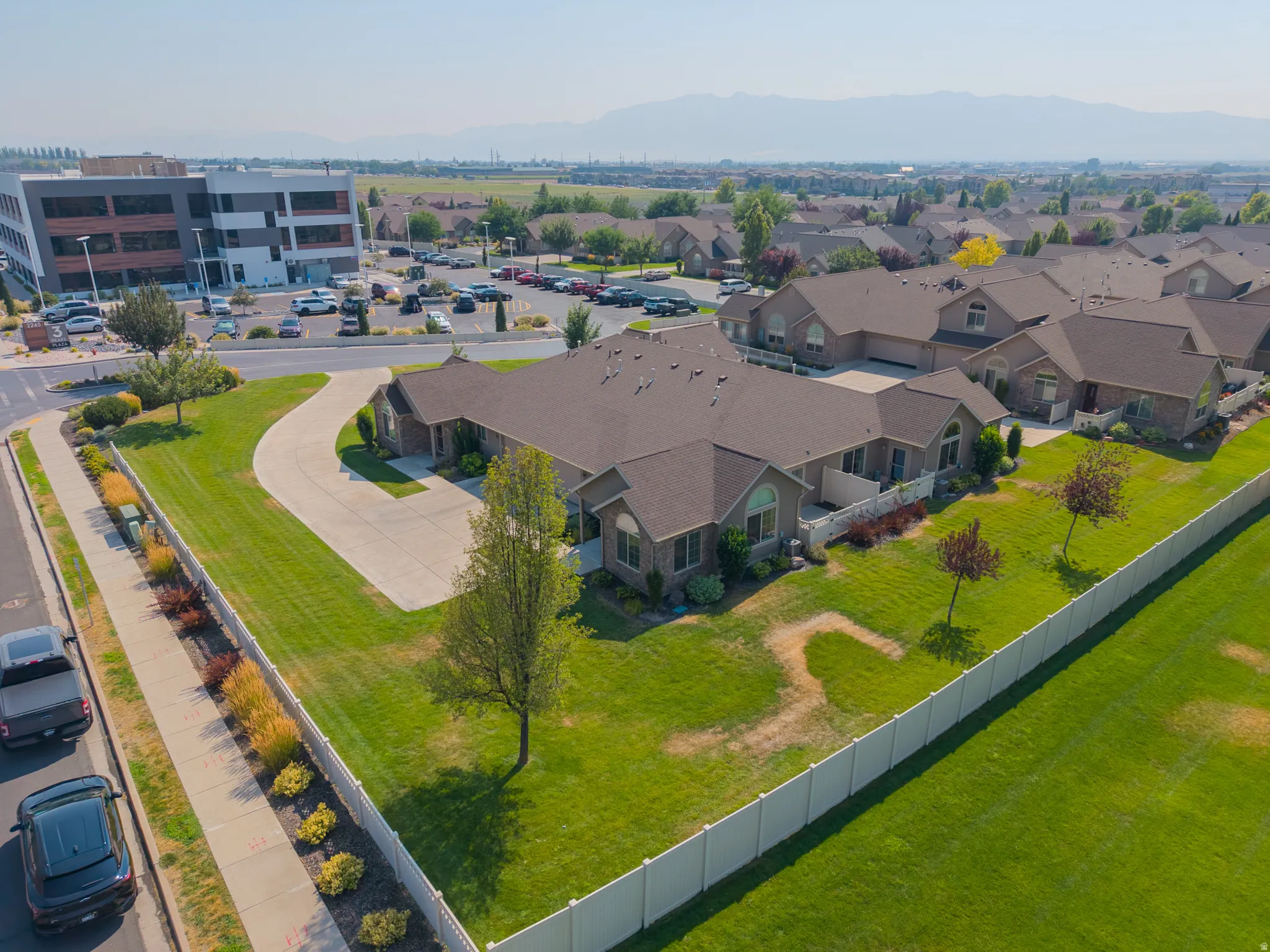Spacious corner lot with extensive green lawn, concrete driveway, and white privacy fencing