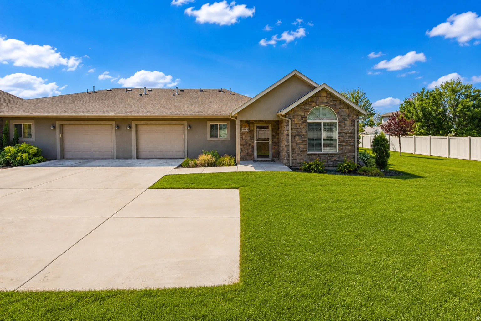 Stone and stucco exterior, arched window detail, two-car garage, concrete driveway, and expansive lawn
