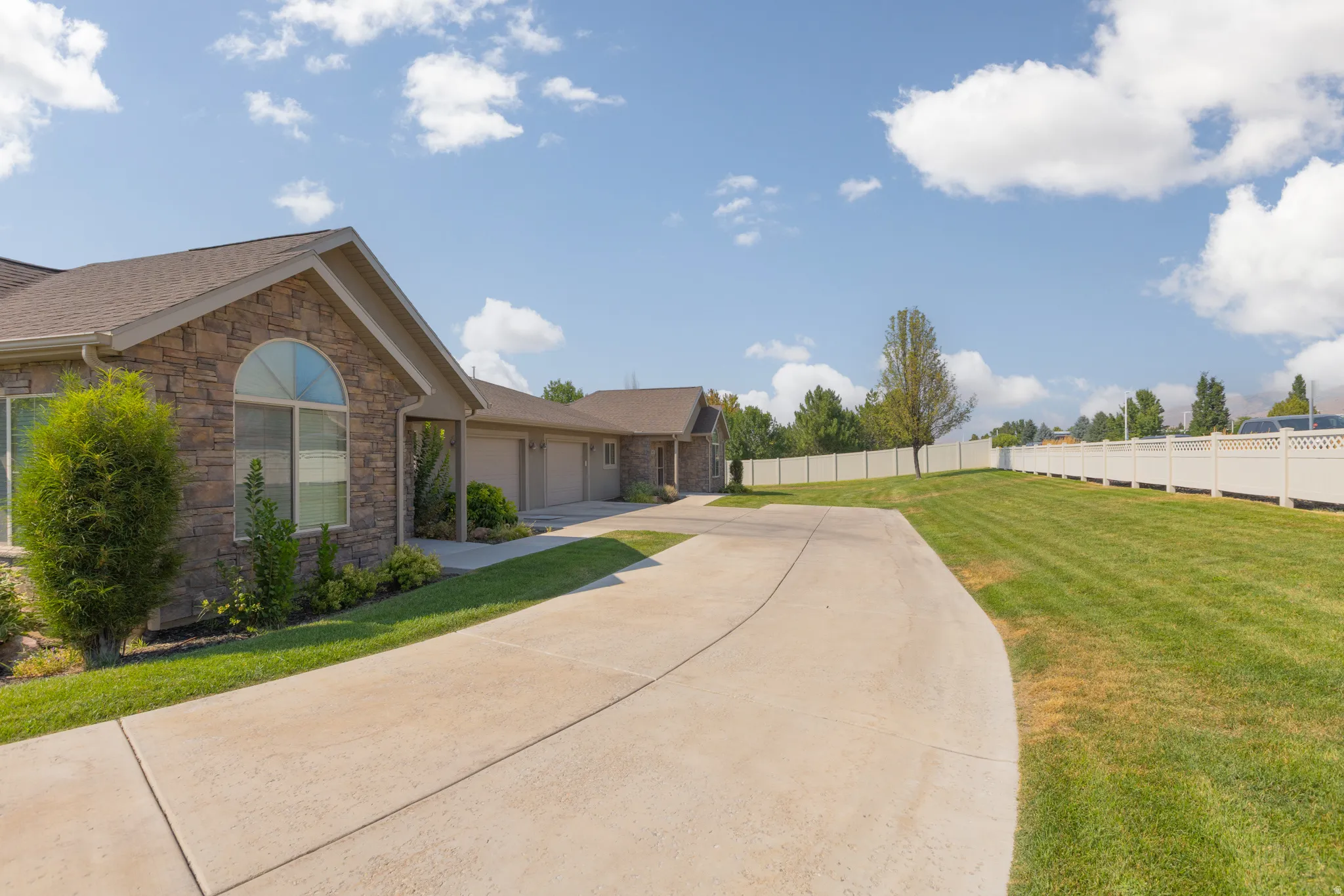 Stone facade exterior with an arched window, a multi-car garage, a concrete driveway, and a white privacy fence