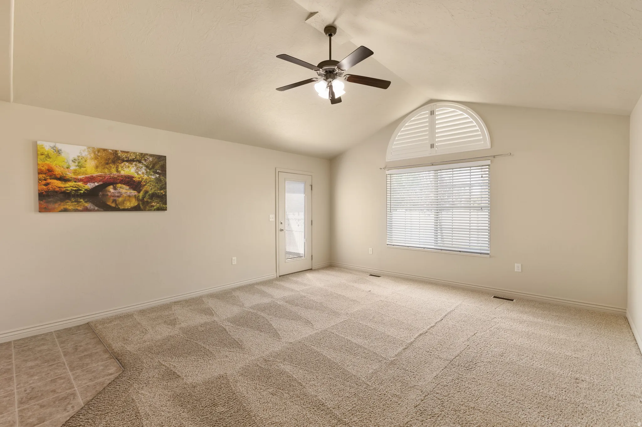 Vaulted ceiling with a ceiling fan, arched window with shutters, glass-paneled door, and patterned carpeting