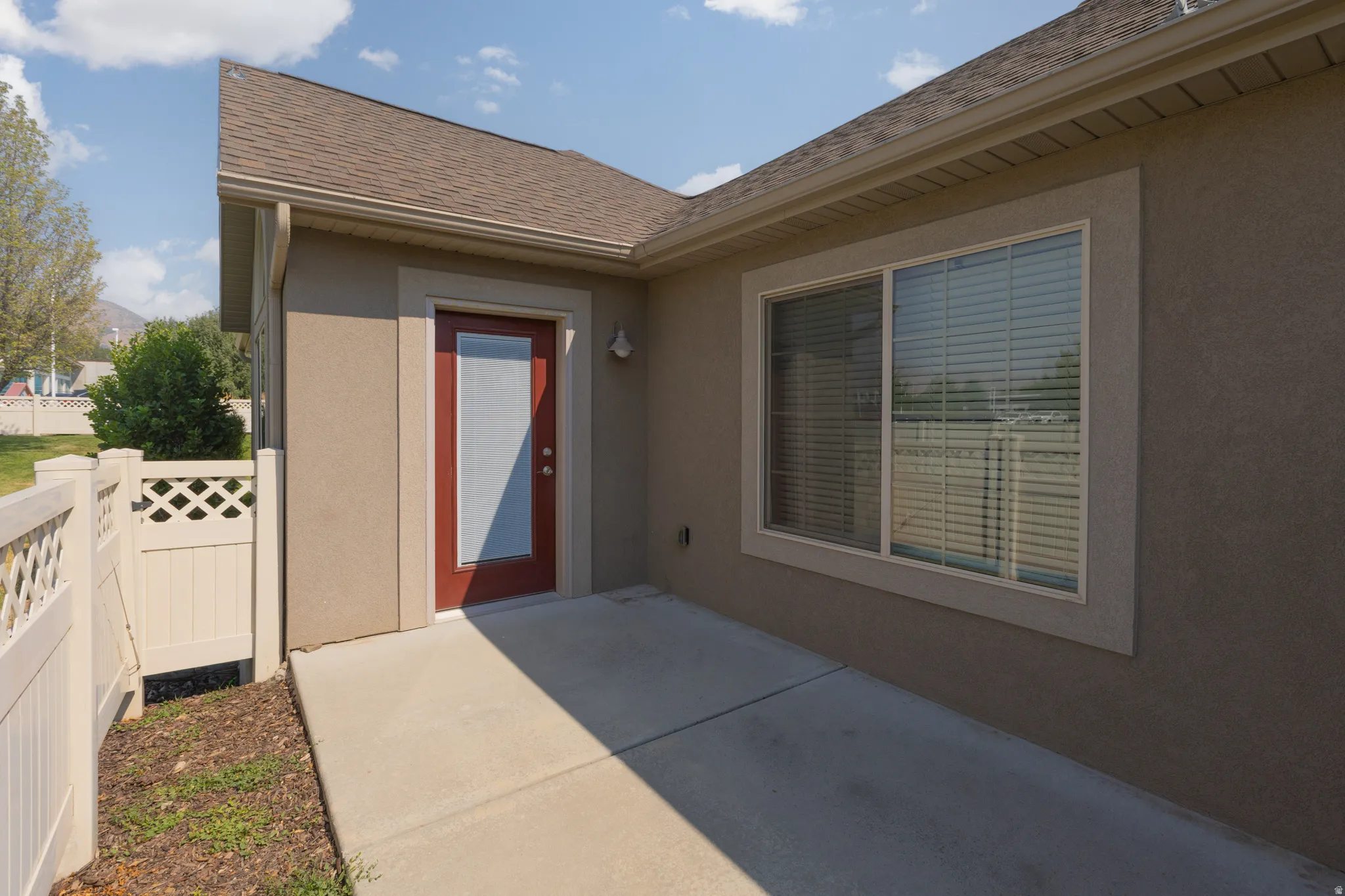 Private patio area featuring a red entry door with frosted glass, exterior wall sconce, and a large sliding window