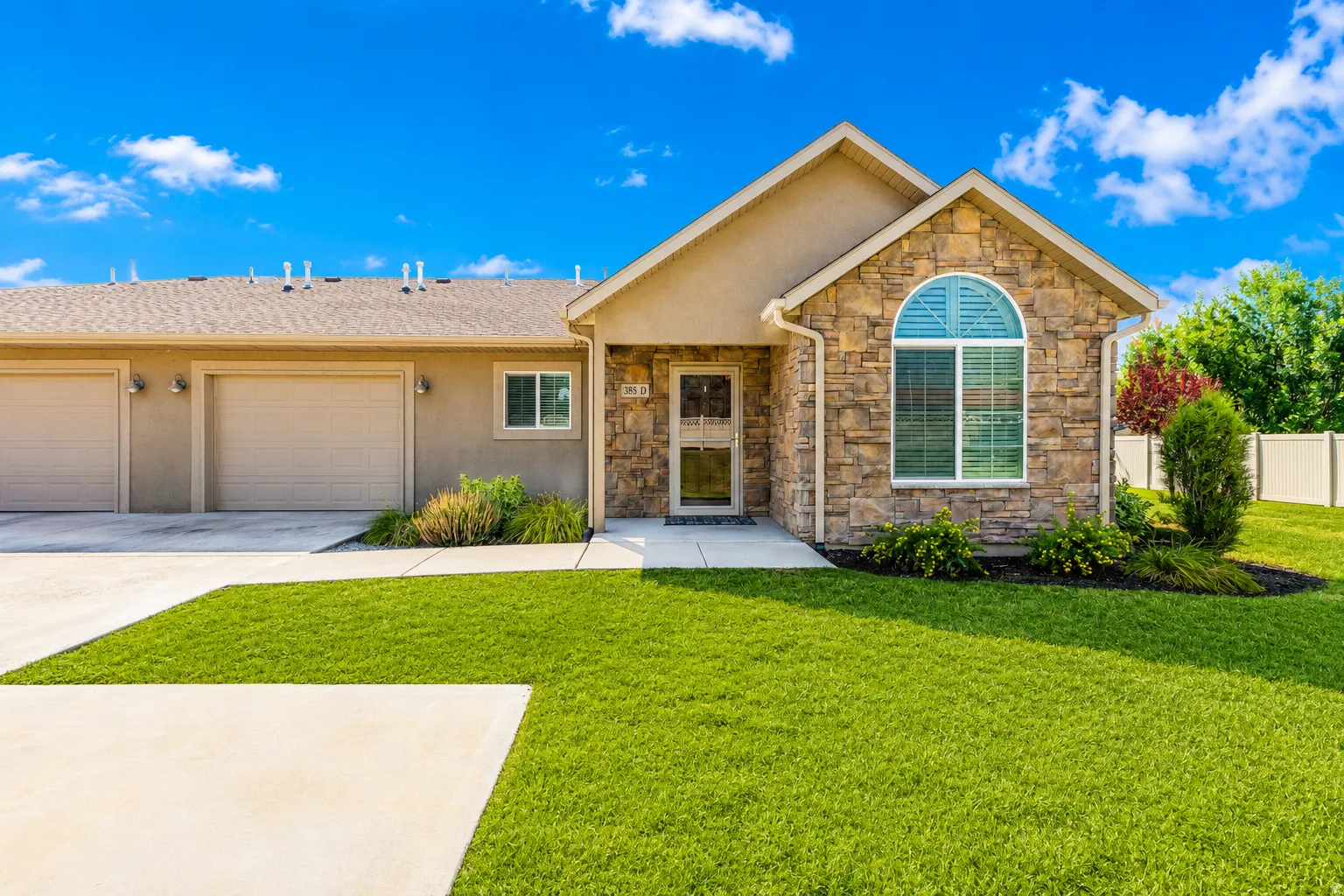 Stone and stucco exterior with an arched window, attached two-car garage, and concrete driveway