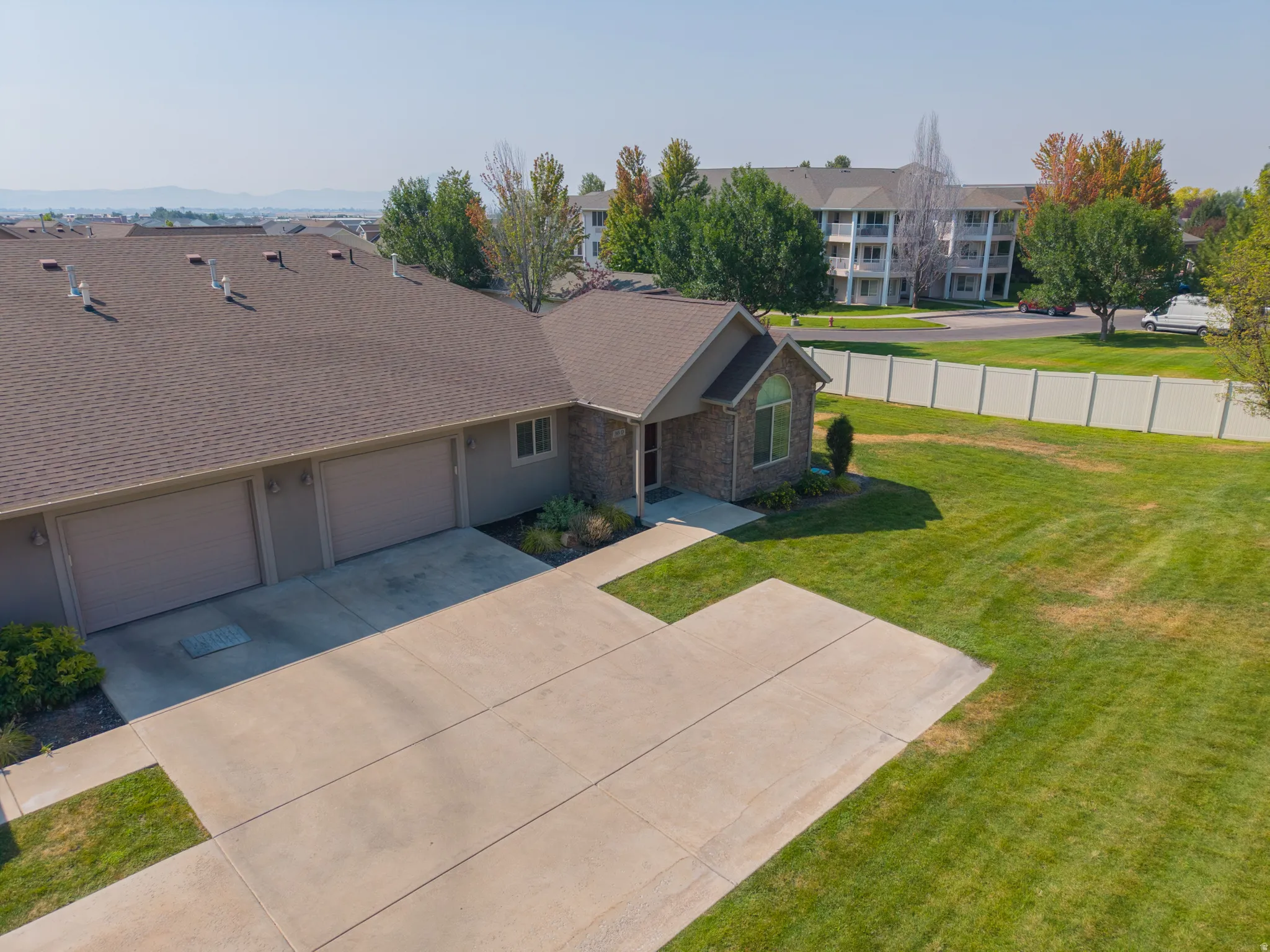 Property exterior featuring a multi-car garage, concrete driveway, stone facade accents, and a fenced yard