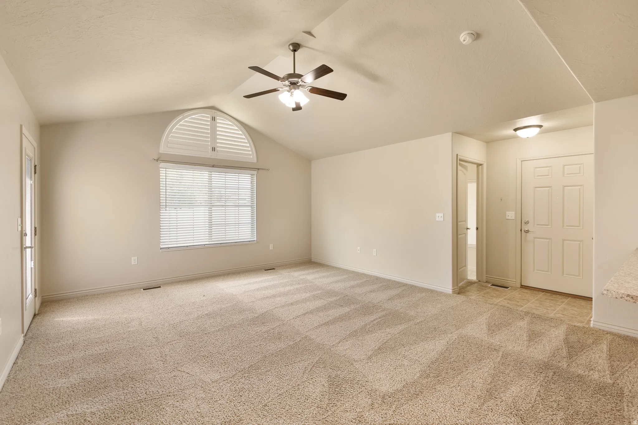 Vaulted ceiling with a ceiling fan, arched window with shutters, and light-toned carpeting