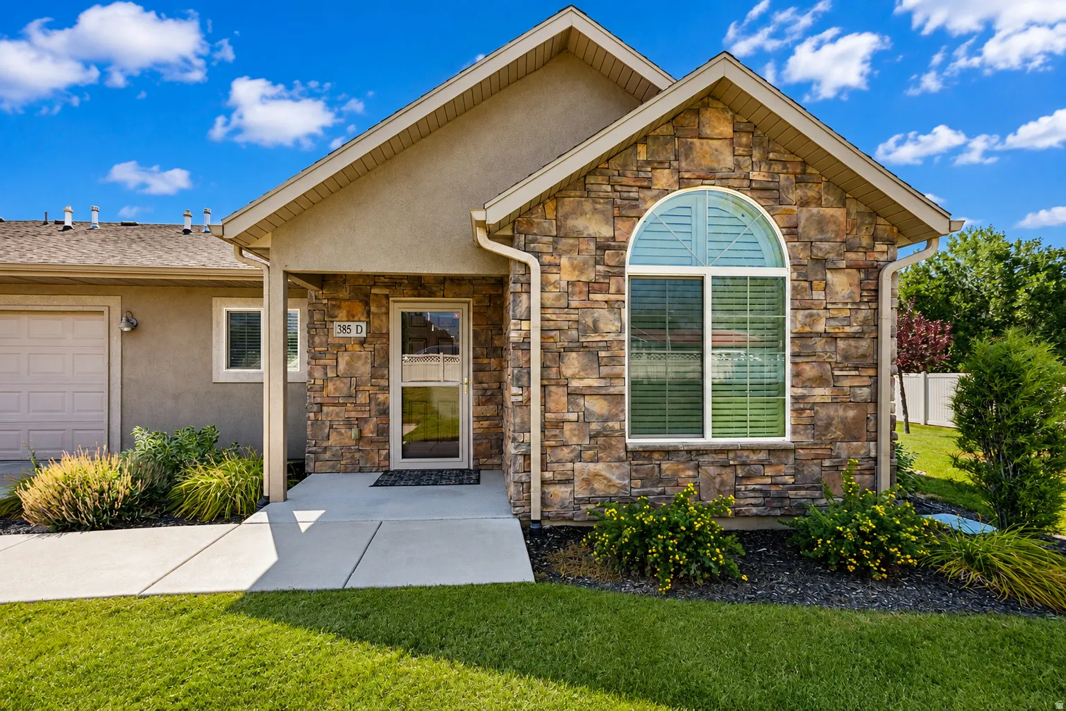 Stone veneer facade with an arched window, stucco siding, and an attached garage