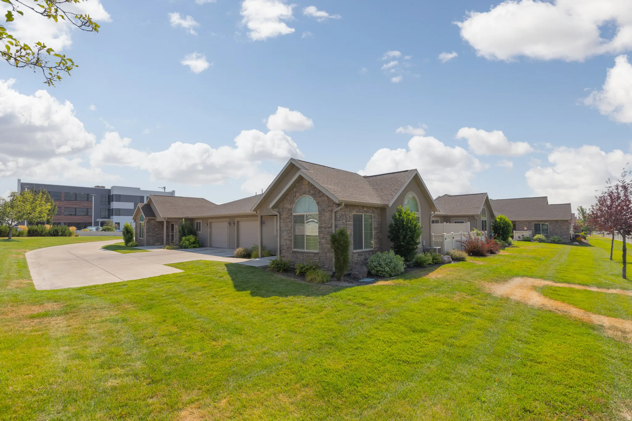 Stone and siding exterior with arched windows, attached garage, concrete driveway, and landscaped grounds