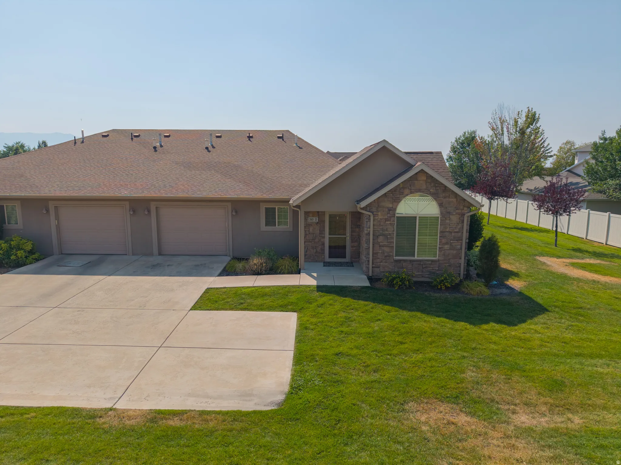 Stone facade with arched window, two-car garage, concrete driveway, and front lawn