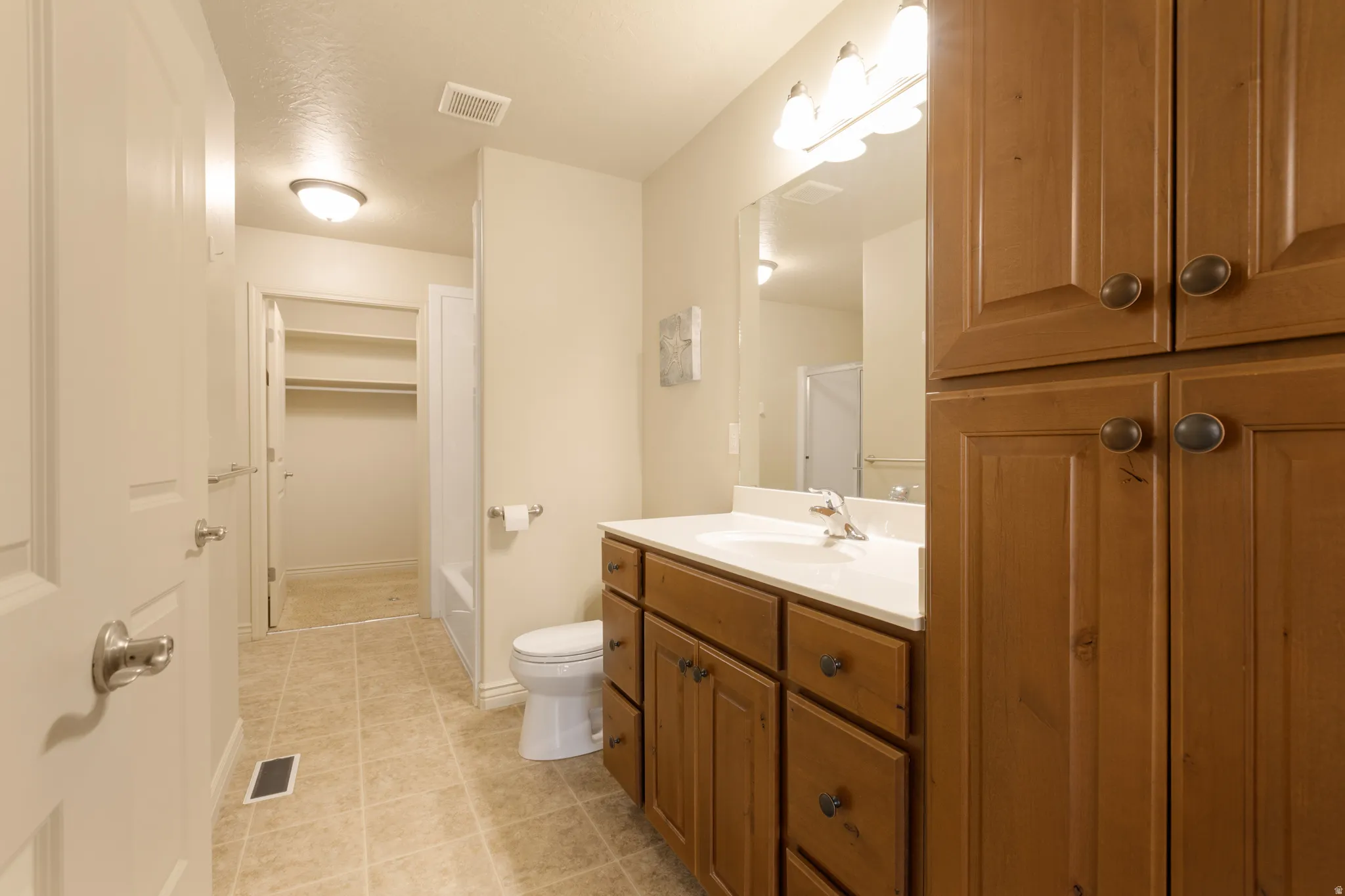 Bathroom featuring wood-finish cabinetry, a single vanity with a white countertop, and tiled flooring