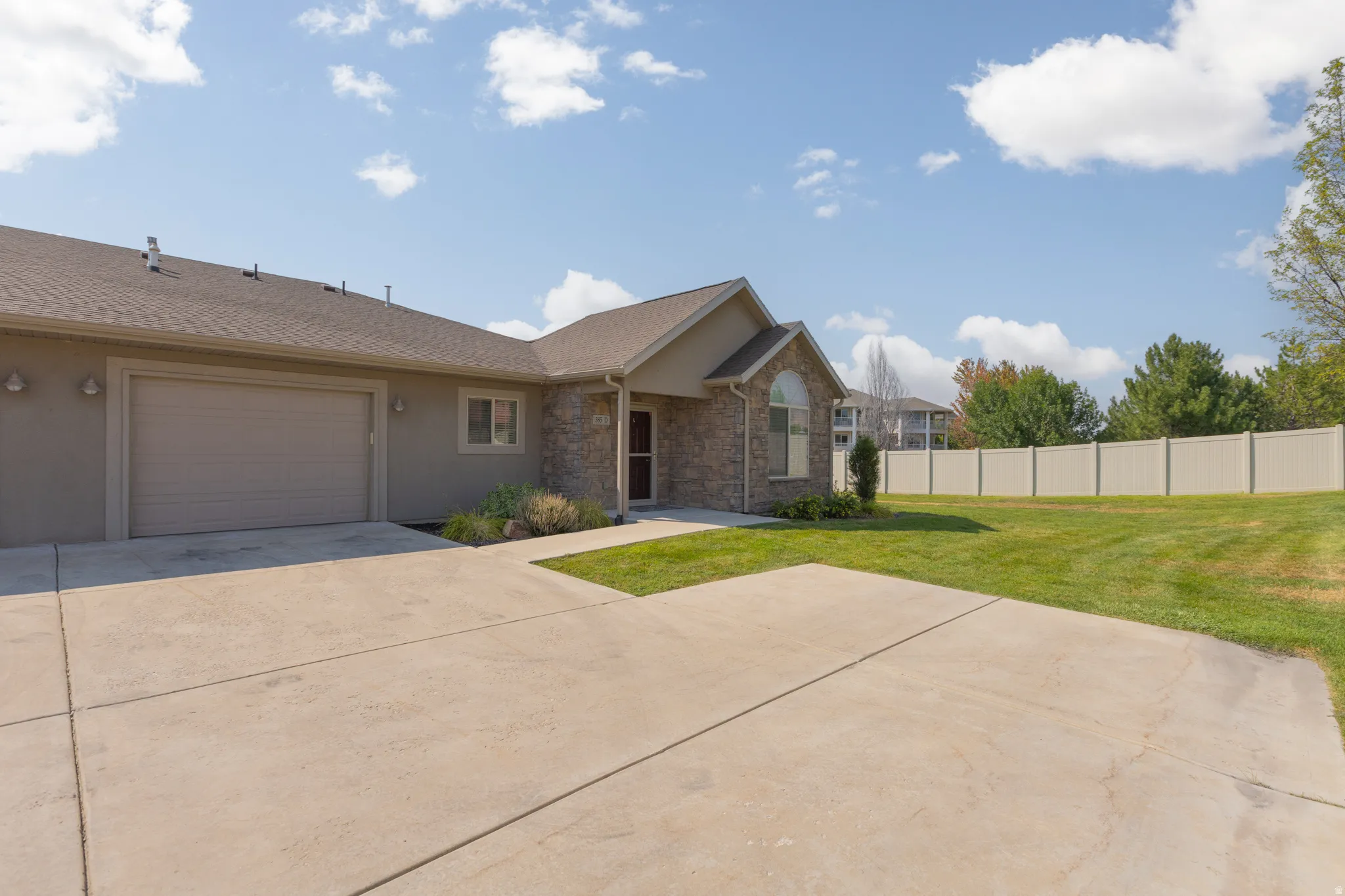 Stucco exterior with stone accents, covered entry, attached garage, concrete driveway, and a fenced yard with established lawn