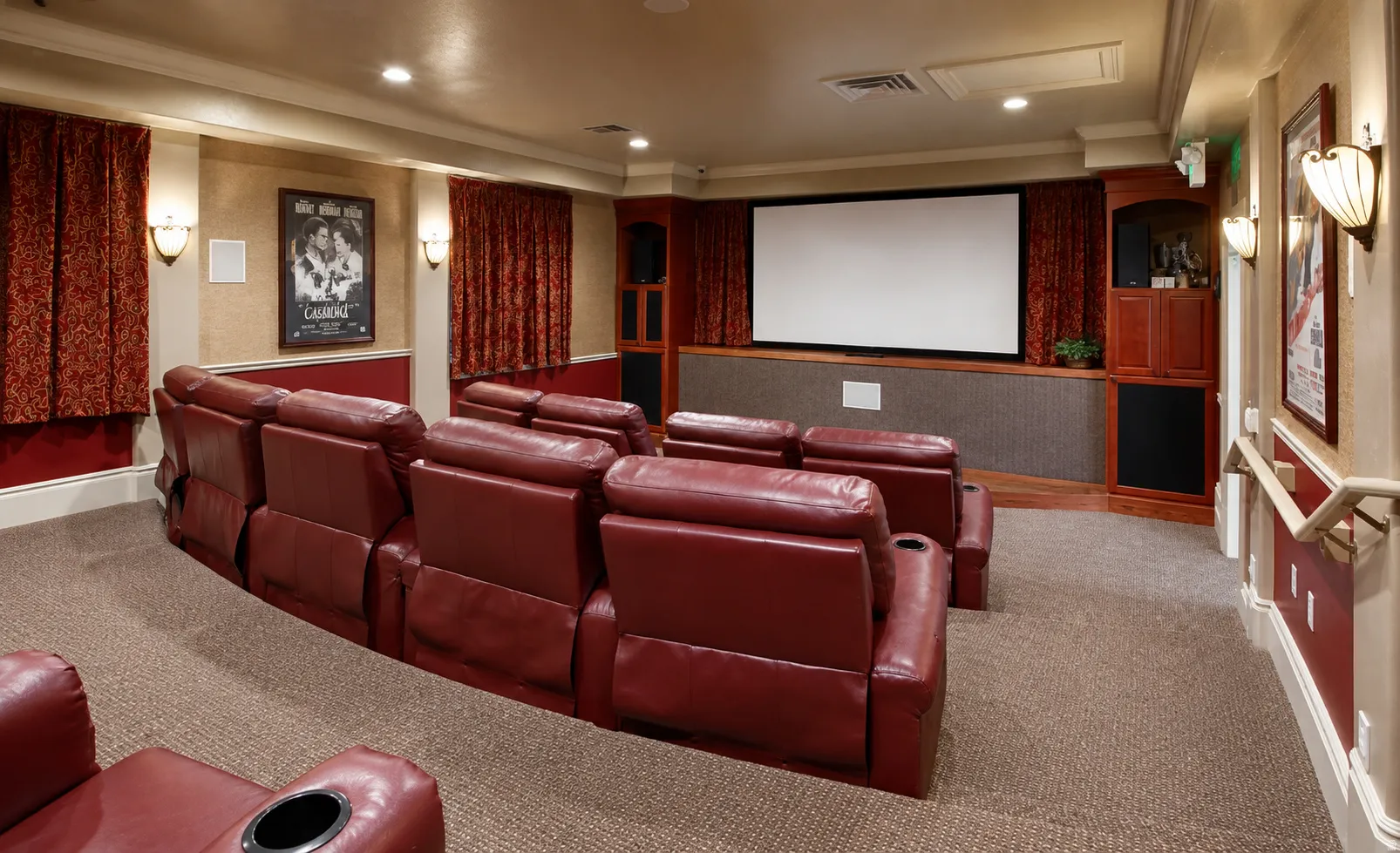 Integrated home theater featuring a large projection screen, dedicated built-in cabinetry, wall sconces, and layered wall treatments