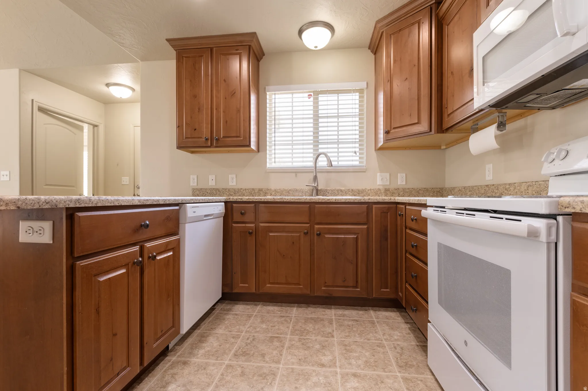 U-shaped kitchen with wood-finish cabinetry, light-colored countertops, and a full suite of white appliances